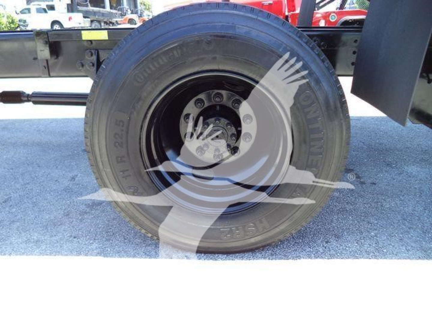 Truck wheel and tire assembly on a 2019 International Durastar 4300 chassis showing large black tire with visible lug nuts and hub, side components, and a reflection of a watermark across the image.