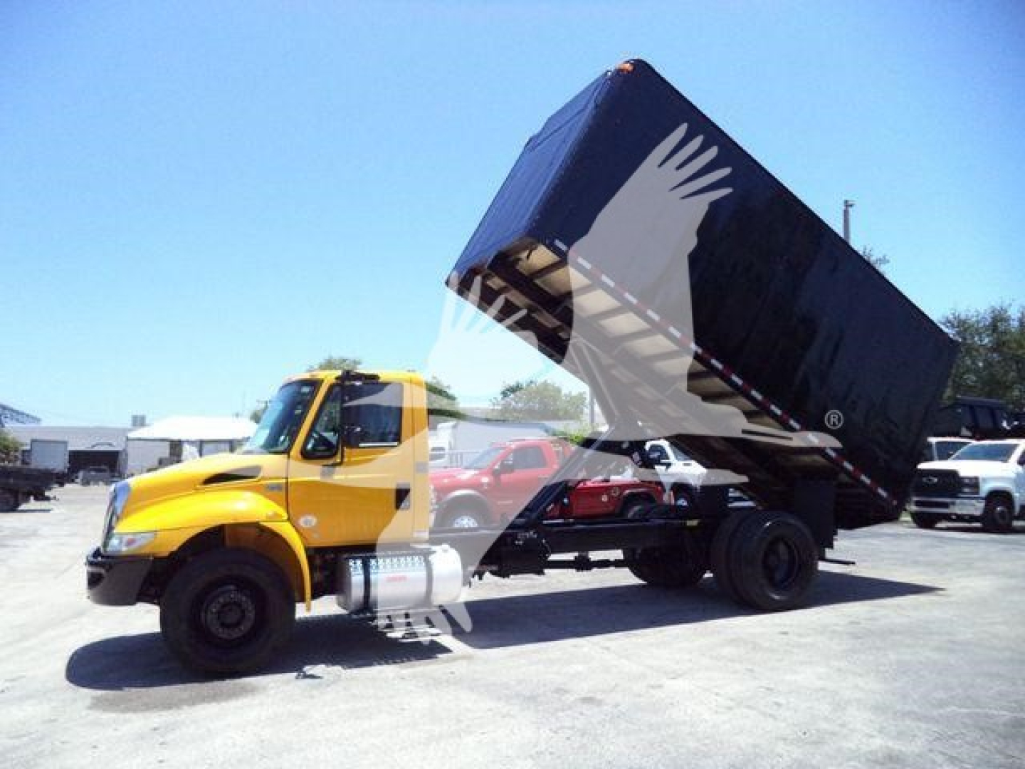 Commercial truck with a yellow International Durastar 4300 cab and a raised dump bed on a tilt-back a-frame, in-sale lot.