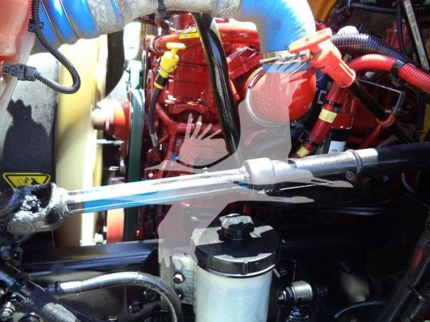 Engine bay of a 2019 International Durastar 4300 showing red engine block, blue hoses, yellow cap, and various cables and components.