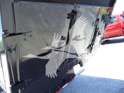 Back view of a black chipper truck body with steel doors and latches, printed graphic of white birds on rear panel.