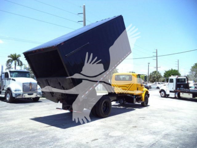 Truck chassis with a raised dump bed showing a black dump container and surrounding vehicles in a lot.