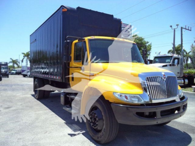 Truck in yard showing yellow 2019 International Durastar 4300 with black cargo container and front grille, side view, daytime sun.