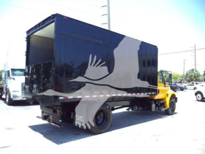 Truck with a dark blue dump body showing a large white silhouette graphic; cargo area open at rear; International Durastar 4300 chassis in yellow.
