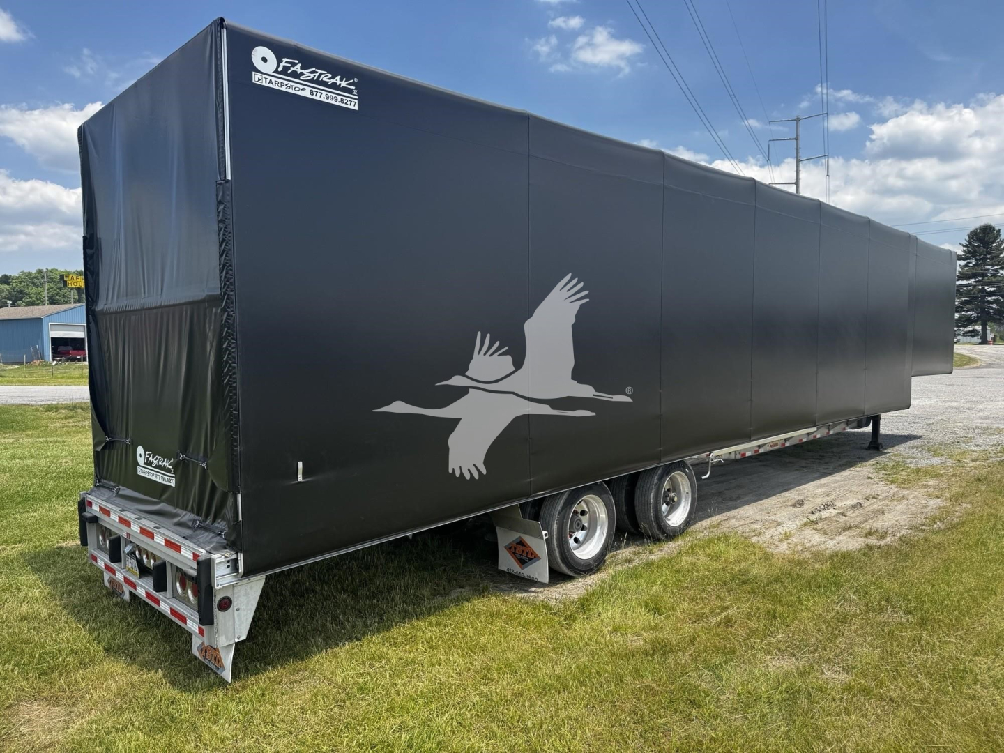 Trailer side view showing black curtain side with a white flying bird logo and rear tail lights.