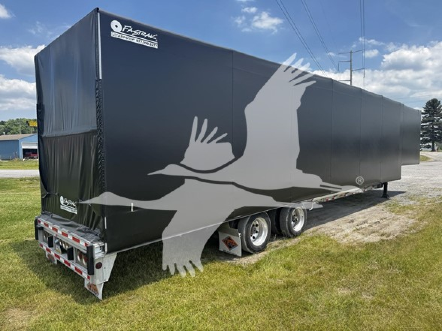 Curtainside trailer in service showing black cover with white bird graphic and dual rear axles.
