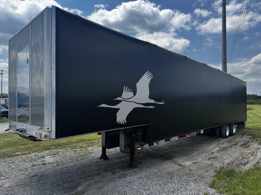 Curtainside trailer showing black exterior with white bird logo on side, rear and landing gear visible.