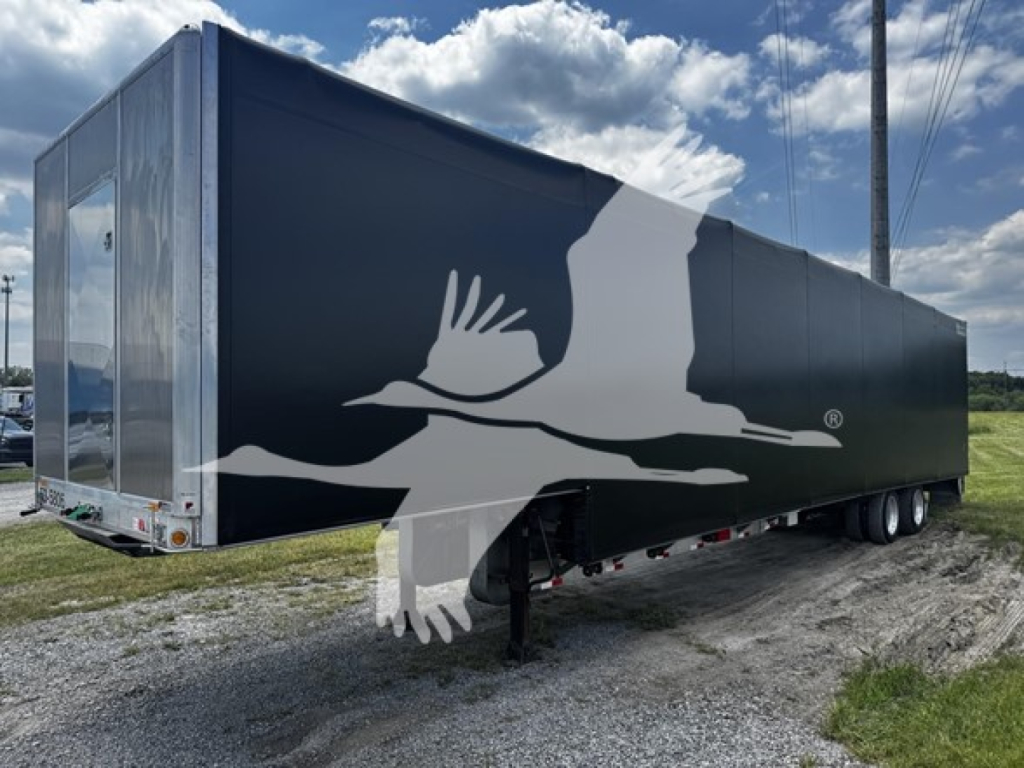 Flatbed-style curtain-sided trailer with black exterior and large white bird graphic on side. Rear and undercarriage visible with triple-axle configuration and landing gear. No readable VIN or labels in close-up.