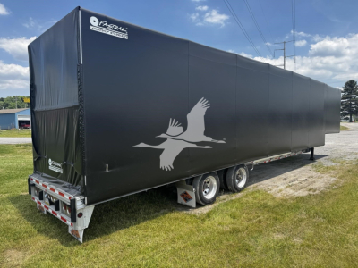 Trailer side view showing black curtain side with a white flying bird logo and rear tail lights.