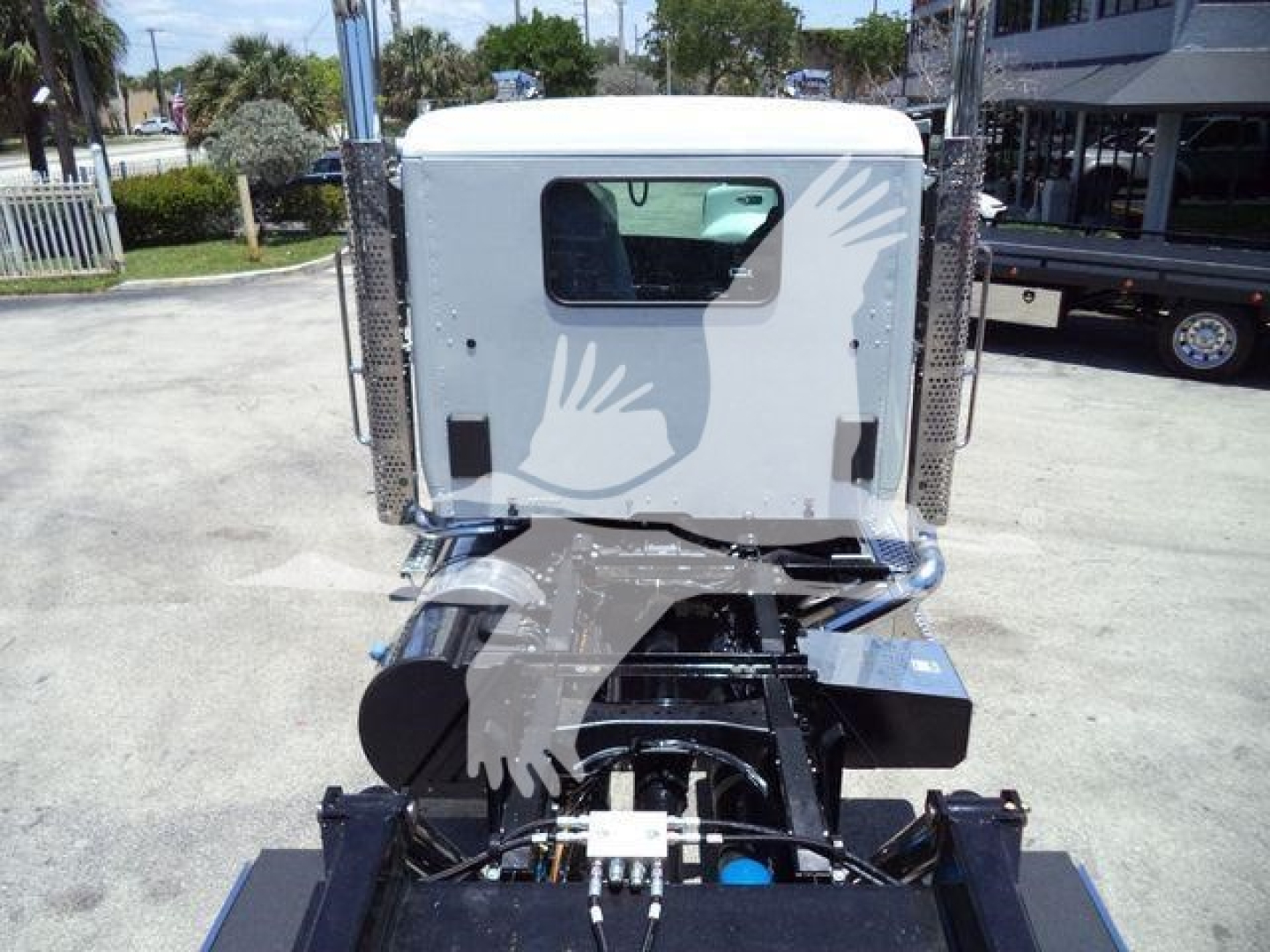 Rear view of a white Kenworth T880 cab on a rollback truck chassis, with exposed engine area and chrome components; no visible text legible on labels.