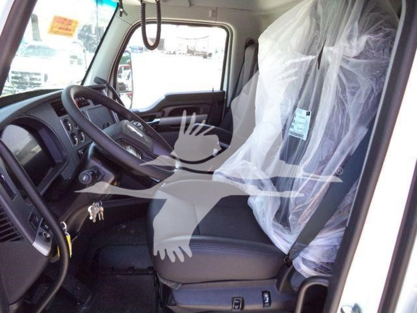 Kenworth T880 truck cabin interior view showing driver's seat, steering wheel, and protective plastic covering on the passenger seat; dashboard and side window visible.