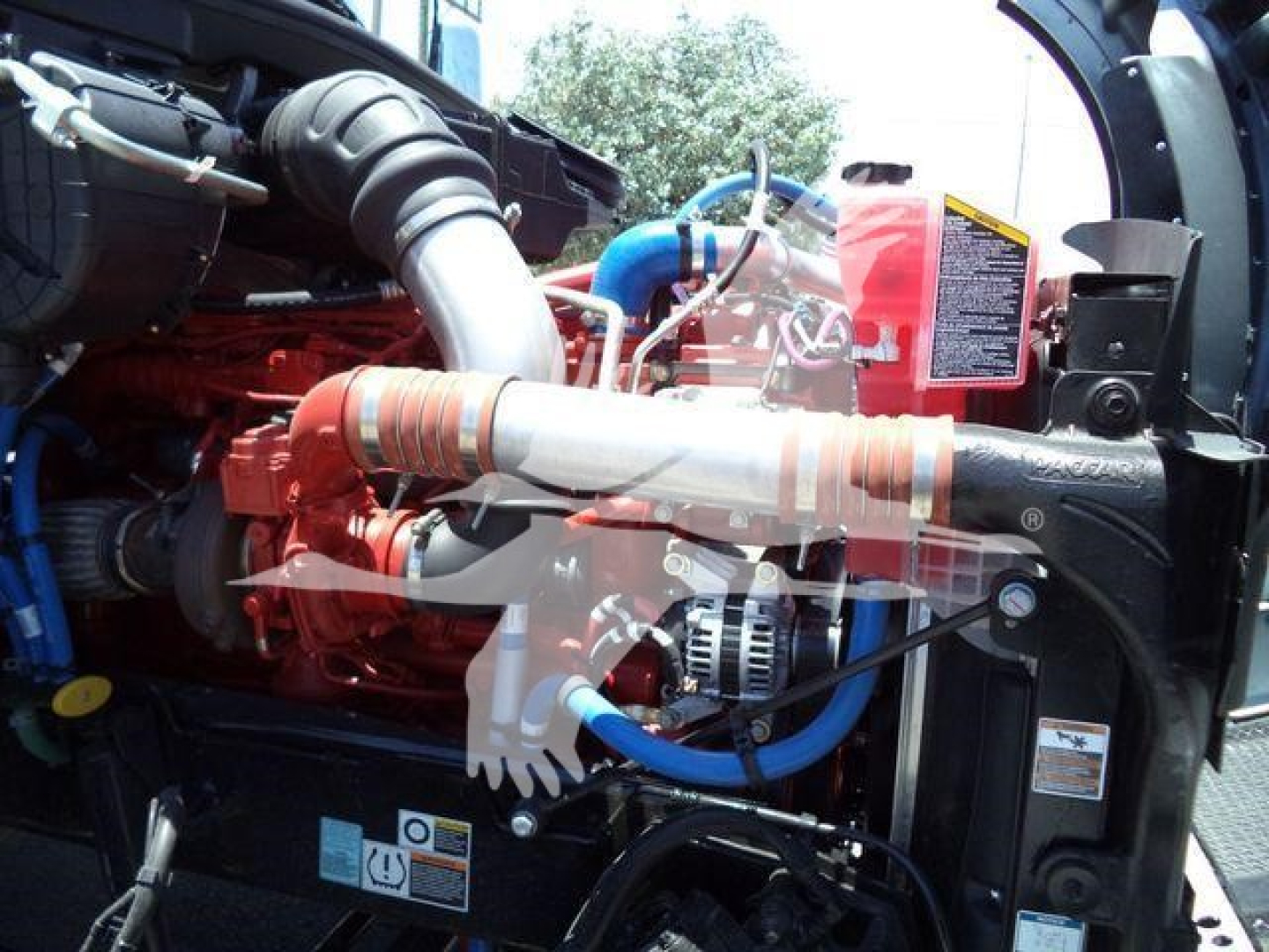Kenworth T880 engine bay with red engine, blue hoses, and silver exhaust, viewed from the front-right showing components and wiring.