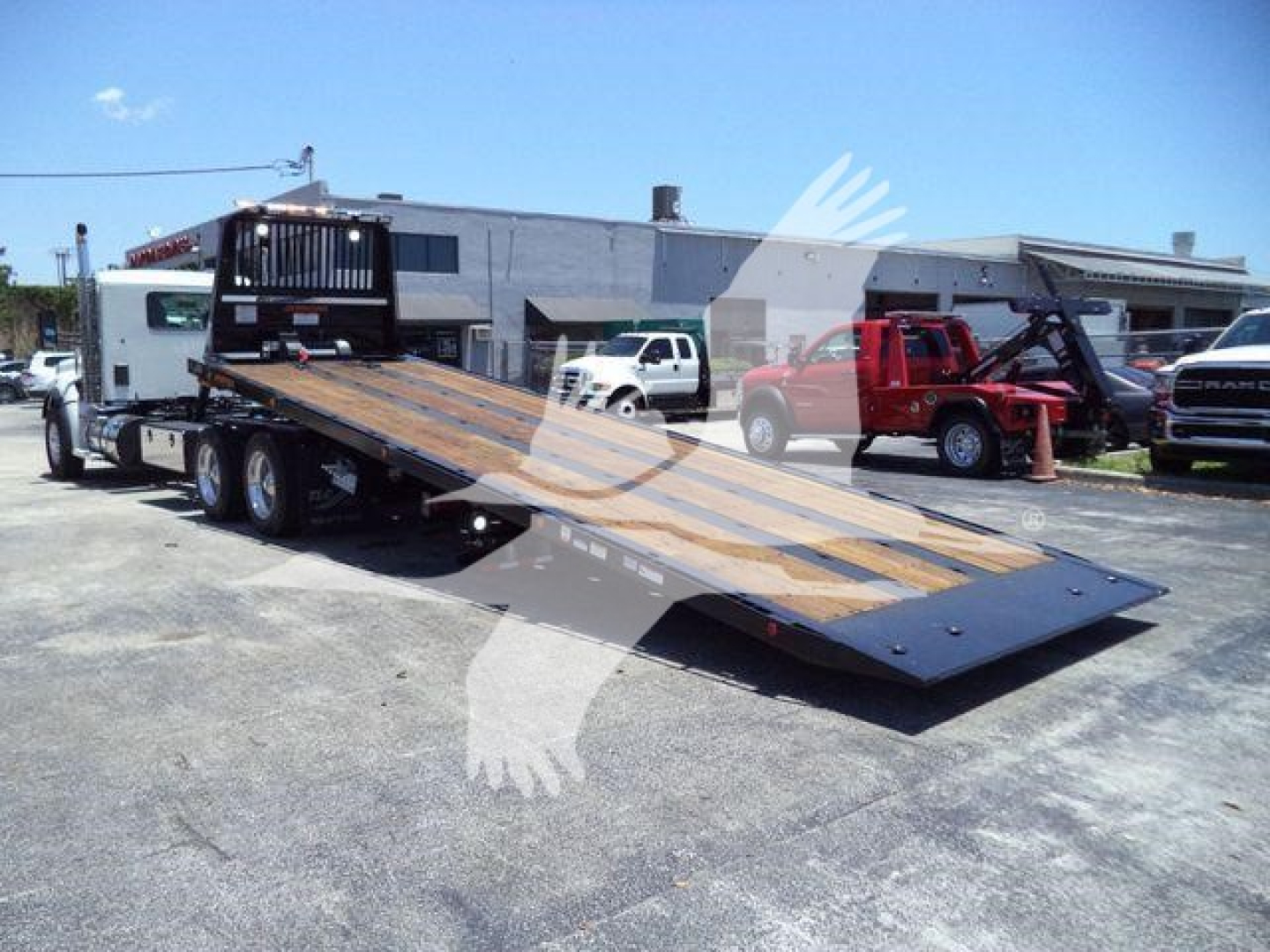 Kenworth T880 rollback truck with flatbed ramp in a dealership lot showing a long wooden deck and metal side rails.