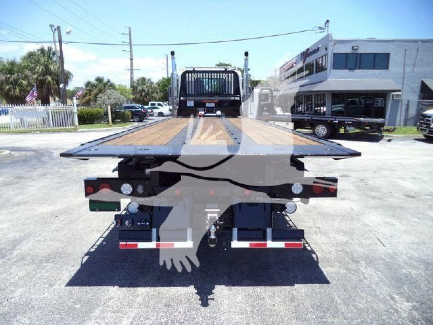 Tow truck flatbed trailer in a dealership lot showing wooden deck and rear lighting.