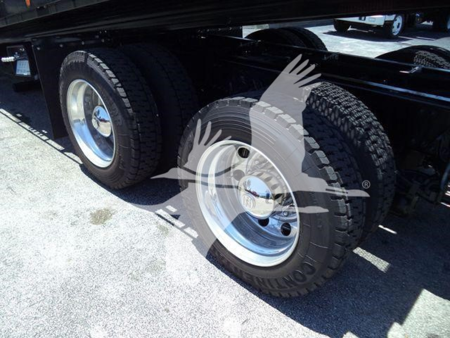Dual rear axles of a blue Kenworth truck with silver wheels and black tires under a trailer.