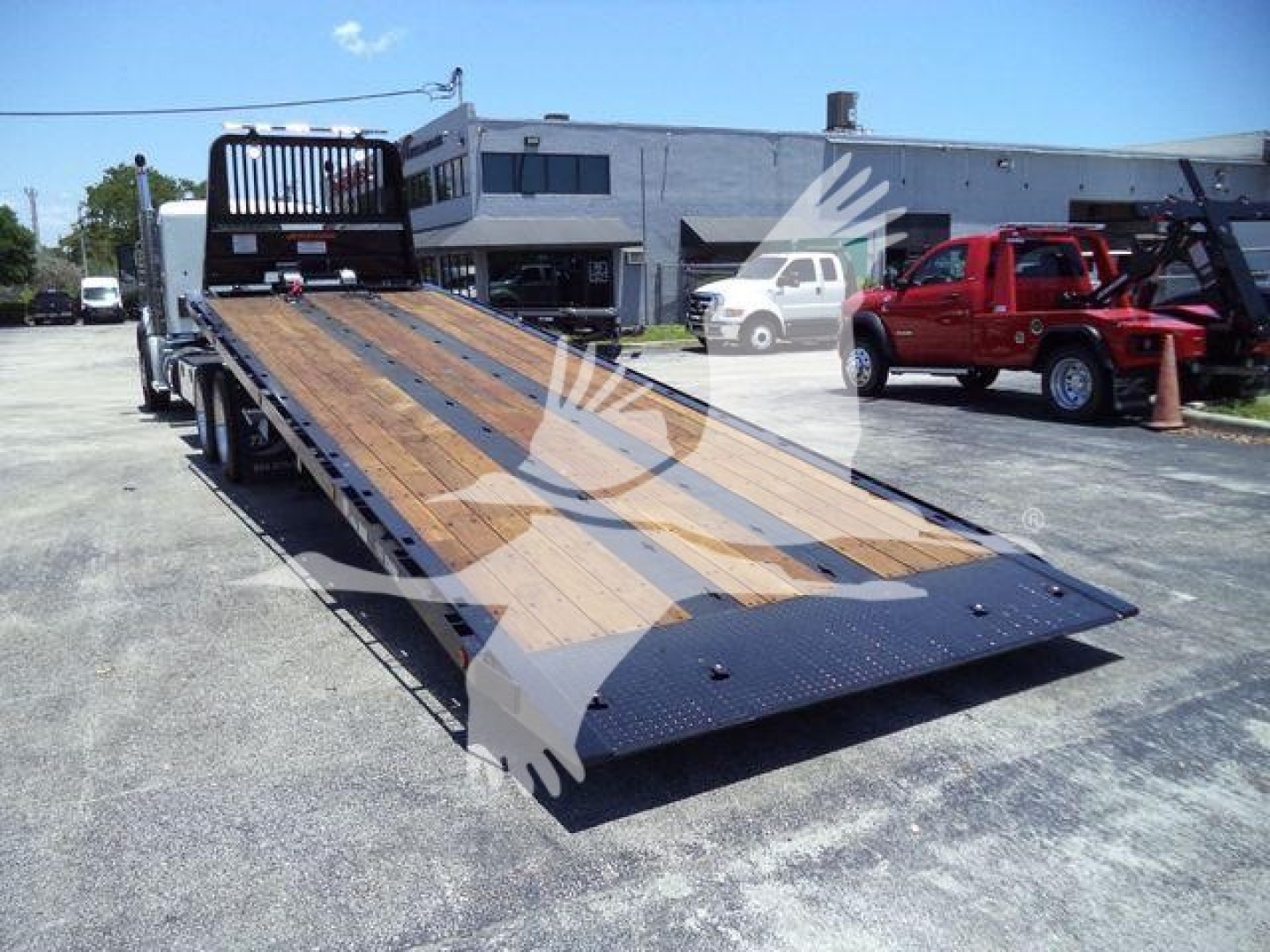 Kenworth T880 flatbed rollback with long wood deck and ramp, viewed from rear-left side in an outdoor lot.