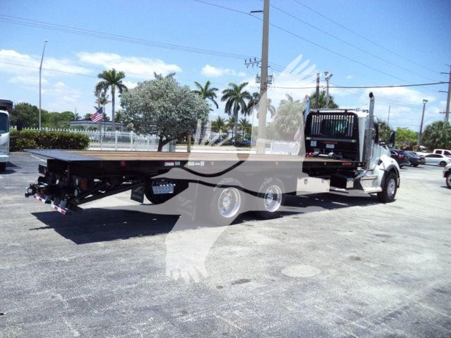 Kenworth T880 rollback truck in a parking lot, flatbed extended, cab with chrome accents, side mirrors, and palm trees in background.