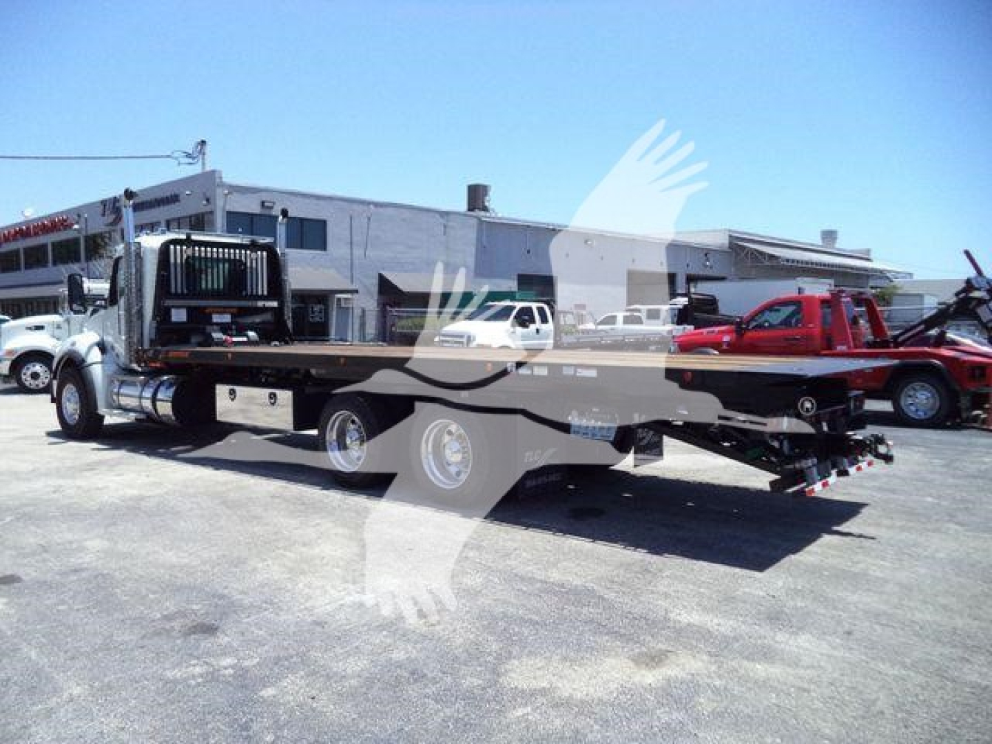Kenworth T880 rollback truck in a dealership lot showing a long flatbed with wheel chocks and equipment, no legible labels visible due to distance.