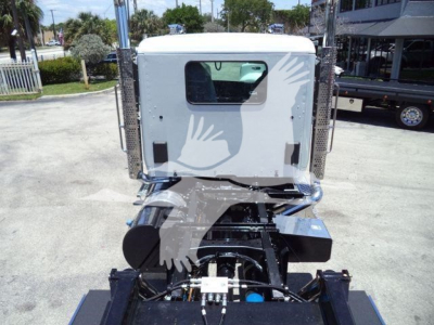Rear view of a white Kenworth T880 cab on a rollback truck chassis, with exposed engine area and chrome components; no visible text legible on labels.