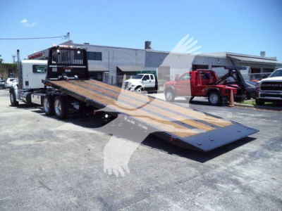 Kenworth T880 rollback truck with flatbed ramp in a dealership lot showing a long wooden deck and metal side rails.