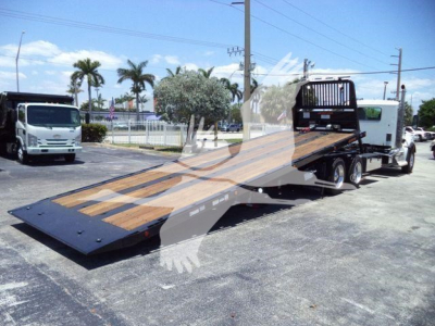Kenworth T880 rollback truck with flatbed, loaded on trailer, cab visible in distance, clear weather.