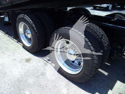 Dual rear axles of a blue Kenworth truck with silver wheels and black tires under a trailer.