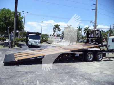 Tractor truck with a lowboy trailer/rollback equipment visible, flatbed ramp extended, Kenworth T880 style cab in distance; no legible labels or text on equipment surfaces.
