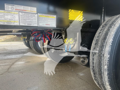 Trailer chassis area showing hydraulic lines and yellow caution label with wheel and underside components visible.