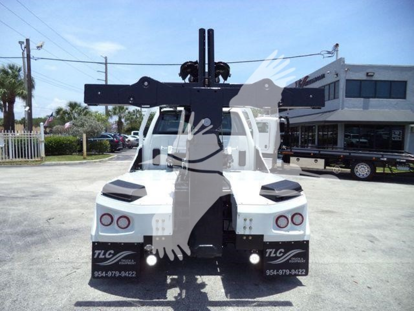 Back view of a white truck with a large overhead winch apparatus/projection mounted on the bed, showing dual taillights and TLC branding on mud flaps.
