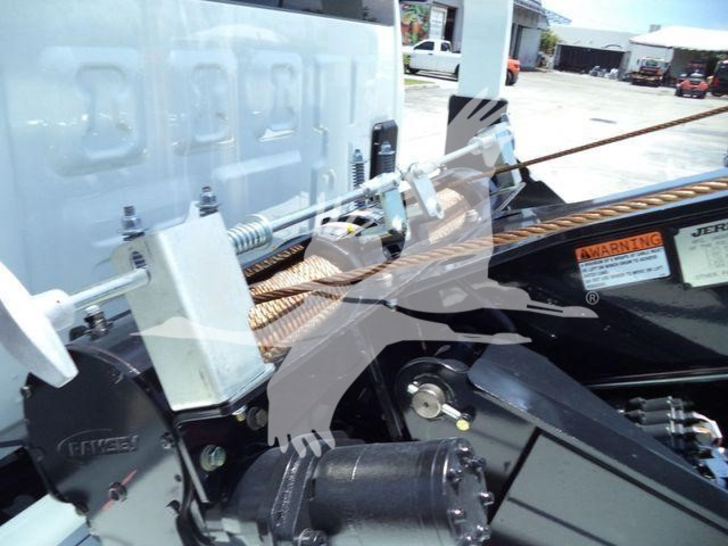 Winch-equipped truck chassis showing hydraulic components and warning label, with metal frame and cables visible.