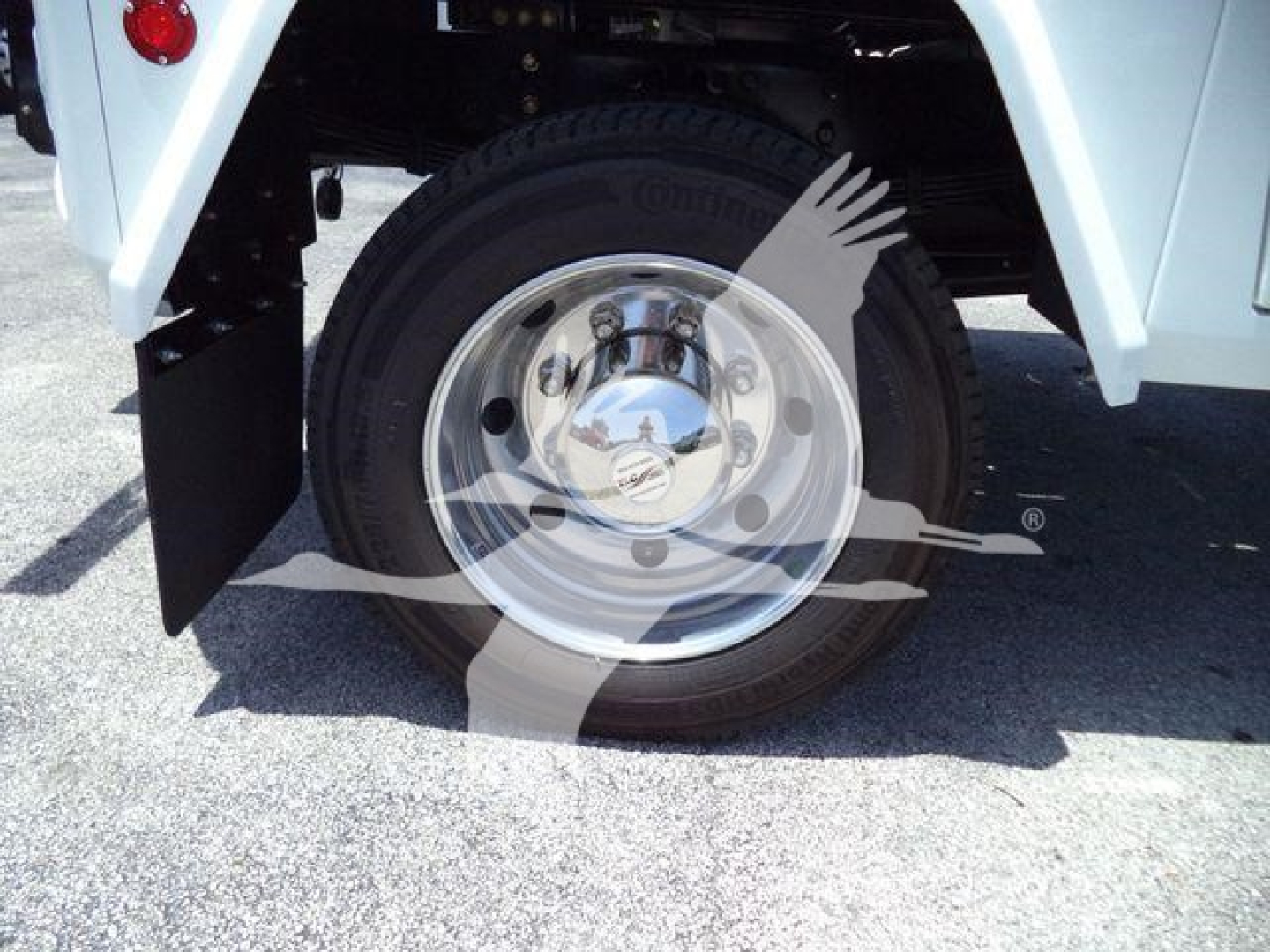 Wheel and hub of a white truck with a chrome wheel, showing a tire and wheel well. A watermark of a hand and gear partially overlays the image.