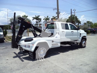 Winch-equipped white 2023 International CV truck side view with heavy front-end hook and crane/winch assembly. Visible text not legible due to distance.