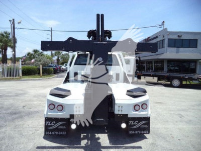 Back view of a white truck with a large overhead winch apparatus/projection mounted on the bed, showing dual taillights and TLC branding on mud flaps.