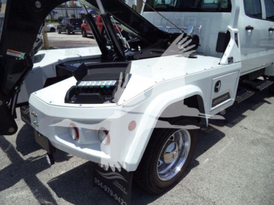 Truck with winch equipment visible on front fender and control panel in flatbed area; white vehicle with black hydraulic arms and chrome wheel hub.