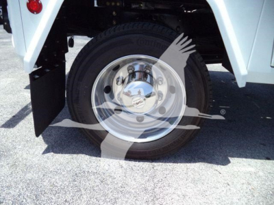 Wheel and hub of a white truck with a chrome wheel, showing a tire and wheel well. A watermark of a hand and gear partially overlays the image.