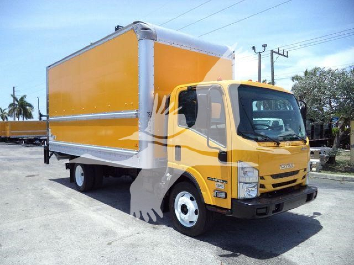 Isuzu NPR HD box truck in-service showing yellow cab and large amber cargo box, front-right view with stock number tag in background.