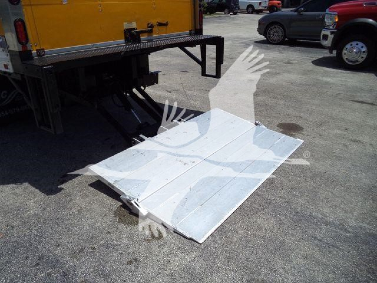 Isuzu NPR HD truck with metal loading ramp/plate extended from bed, aluminum fold-out surface on ground near rear of truck.