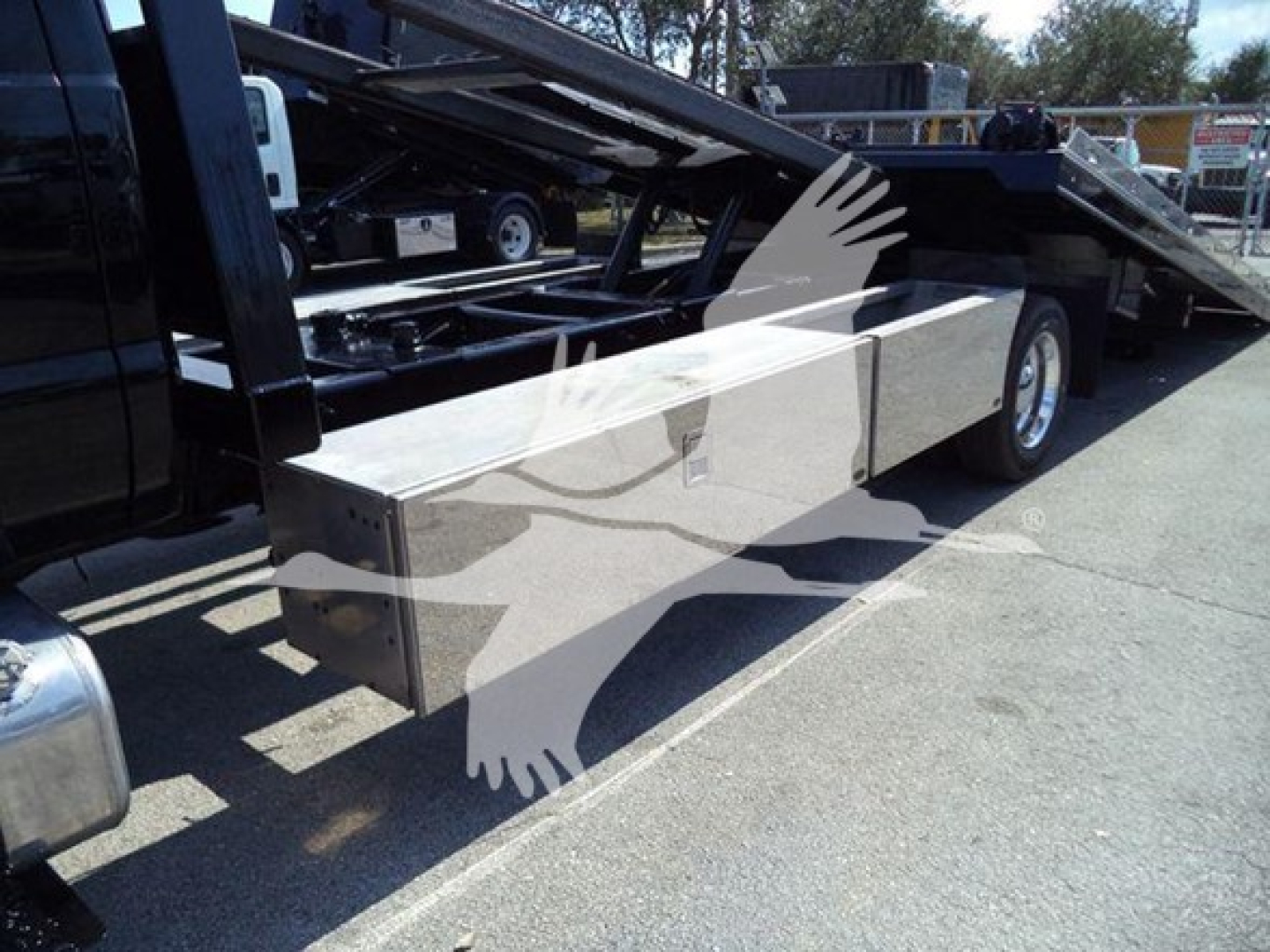 Ford F-650 rollback truck side view showing aluminum storage compartments along the frame and hydraulic tilt bed with winch area.