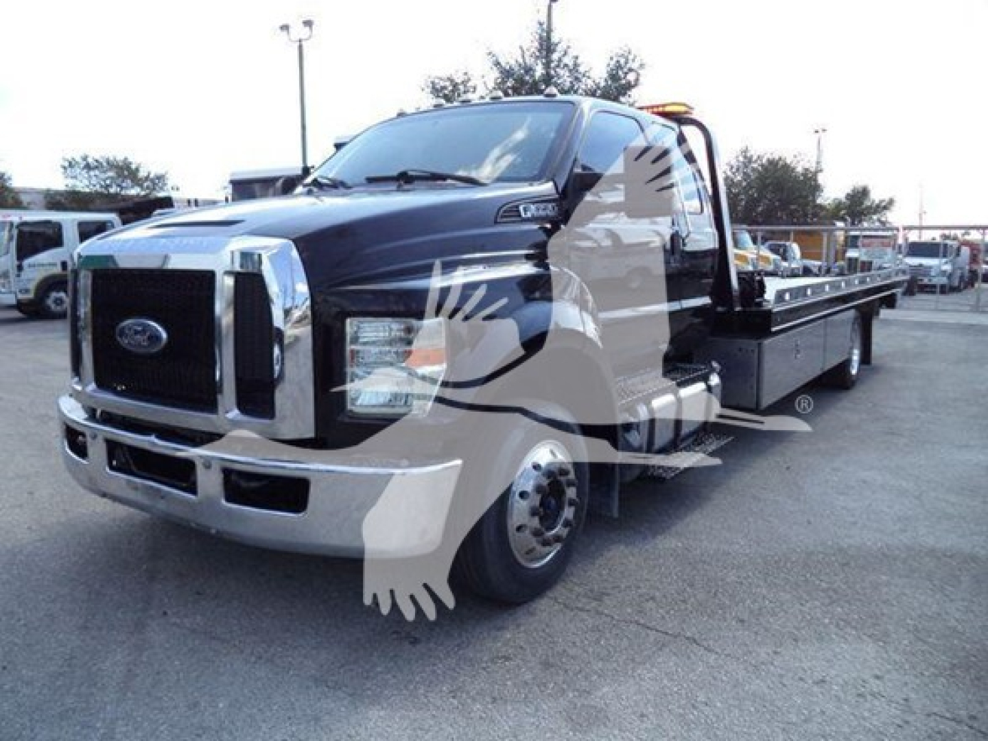Ford F-650 rollback tow truck in dark blue with flatbed, front grille and bumper visible, side view shows extended cab and flatbed with toolboxes.