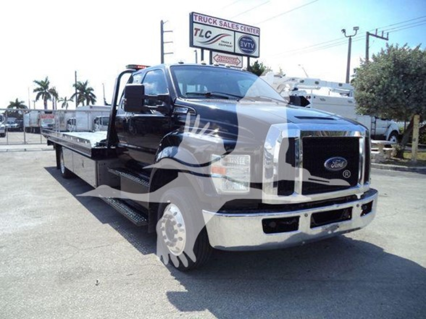 2017 Ford F650 rollback truck with a long flatbed, black cab, chrome front bumper, large grille, and side steps. visible text includes signage in background; no legible model details on the truck body.