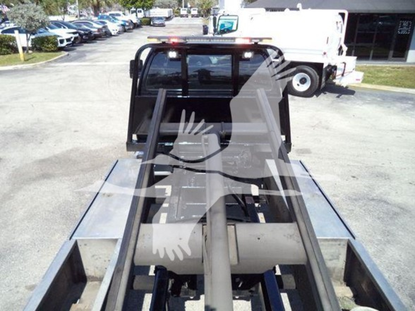Ford F650 rollback truck bed with hydraulic arms and flatbed slots visible from rear; cab window and surrounding equipment in the background.