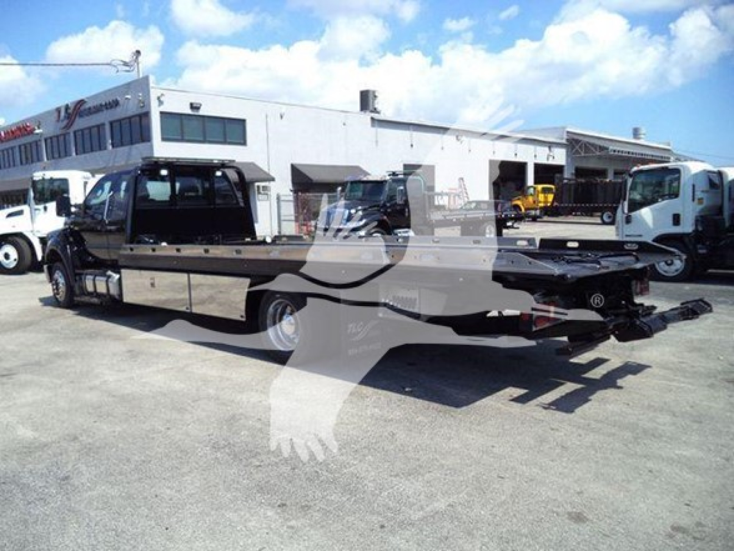 Ford F650 rollback truck in a lot, side view showing extended flatbed with tow equipment and tag axle, truck cab in front.