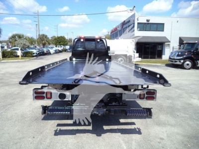 Flatbed tow truck bed rear view showing heavy-duty steel platform and taillights, Ford F-650 rollback, dealership lot in background.