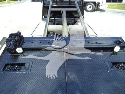 Truck bed of a 2017 Ford F650 rollback showing diamond plate surface and tow hitch area, with hydraulic wheel lift mechanism visible in the background.