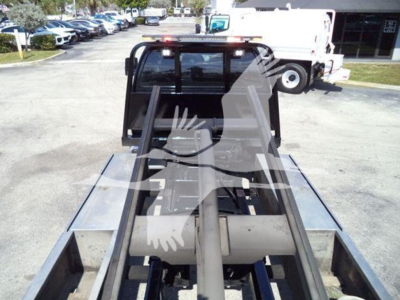 Ford F650 rollback truck bed with hydraulic arms and flatbed slots visible from rear; cab window and surrounding equipment in the background.