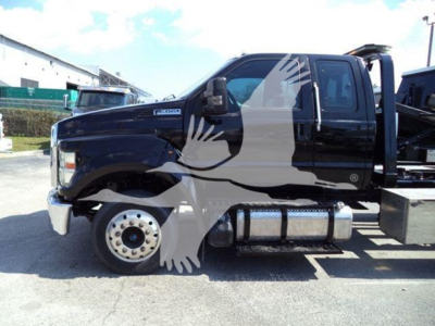 Ford F650 rollback truck side view showing dual rear wheels, black cab, chrome bumper, and fuel tanks visible under cabin.