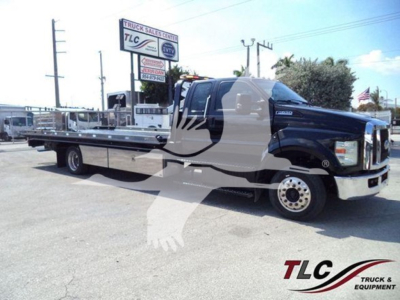 Ford F650 rollback truck showing flatbed with black cab and chrome front, VIN 1FDWX6DE8HDB06405 on bumper, TLC Truck Sales Center sign in background.