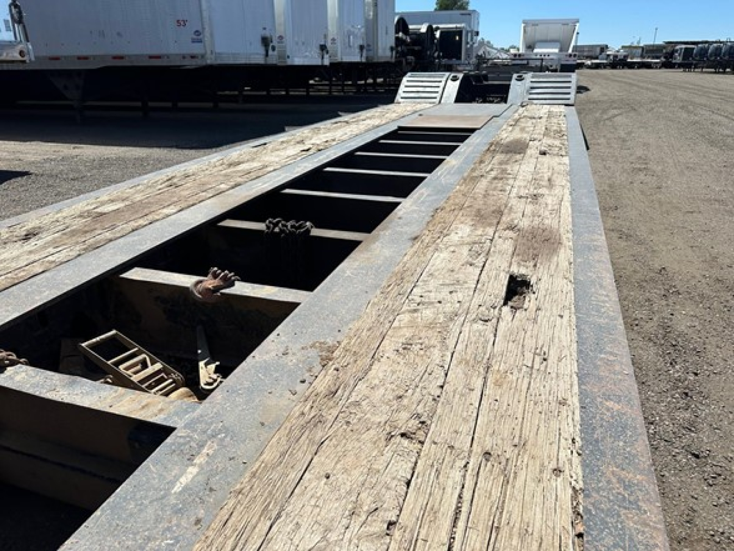 Trail King 50 Ton lowboy trailer deck with wooden planks and metal frame, open central channel with catwalk grates at far end; visible wear marks.
