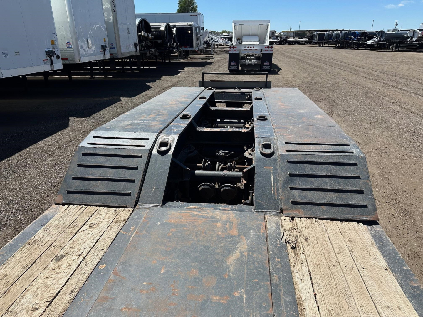 Trail King lowboy trailer deck with pony motor wells and heavy steel ramps, 50 ton capacity, center viewed from rear showing winches and mechanical components.