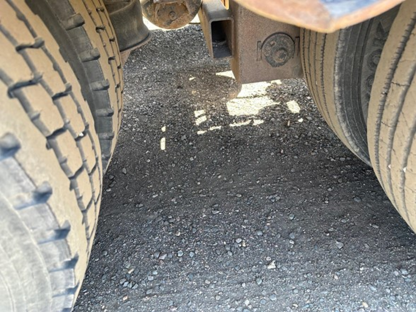 Underneath a 50 ton lowboy trailer showing dual rear axles and a center frame with a circular hitch component.