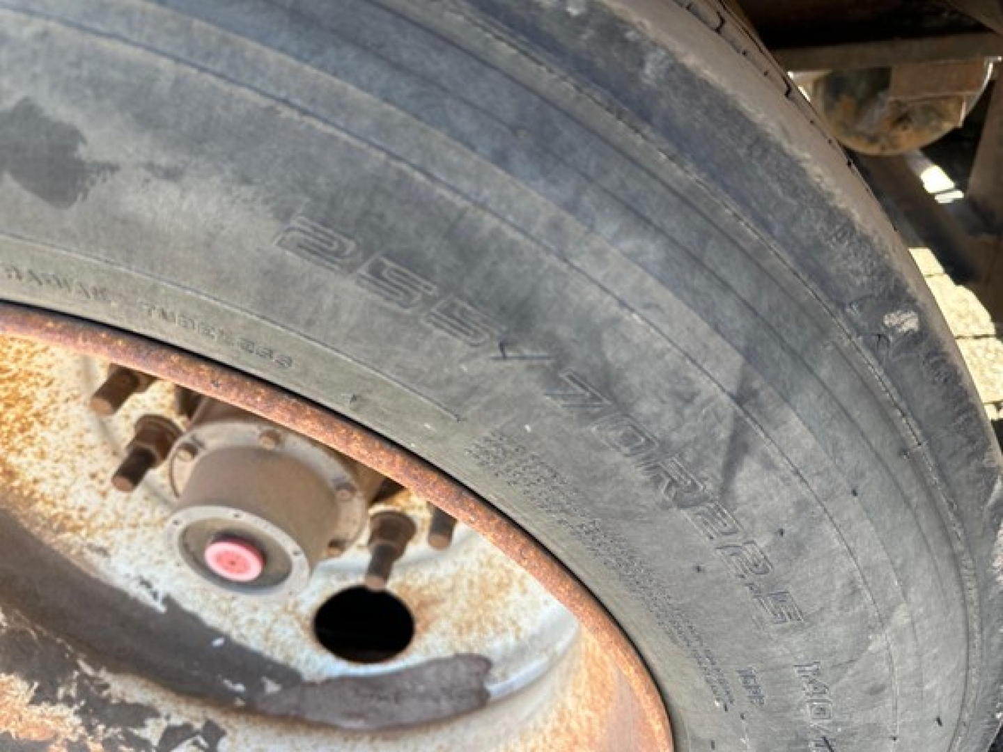 Trail King 50 ton lowboy trailer wheel end showing tire with embossed text and rusty wheel hub.